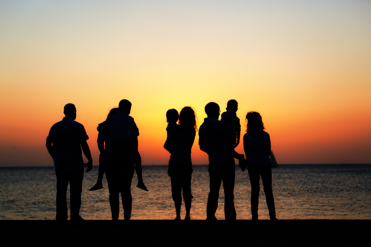Silhouettes of family standing on a beach at sunset.
