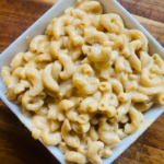 A bowl of Best Healthy Instant Pot Mac and Cheese in a white square bowling sitting on a wooden cutting board. You should make this recipe!