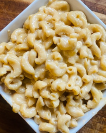 A bowl of Best Healthy Instant Pot Mac and Cheese in a white square bowling sitting on a wooden cutting board. You should make this recipe!